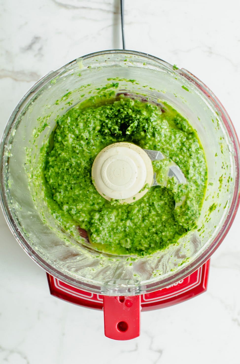 An overhead shot of a food processor with basil pesto inside.