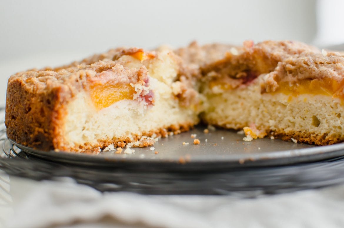 A close up shot of a peach crumb coffee cake with a few slices removed to show the inside texture of the cake. 