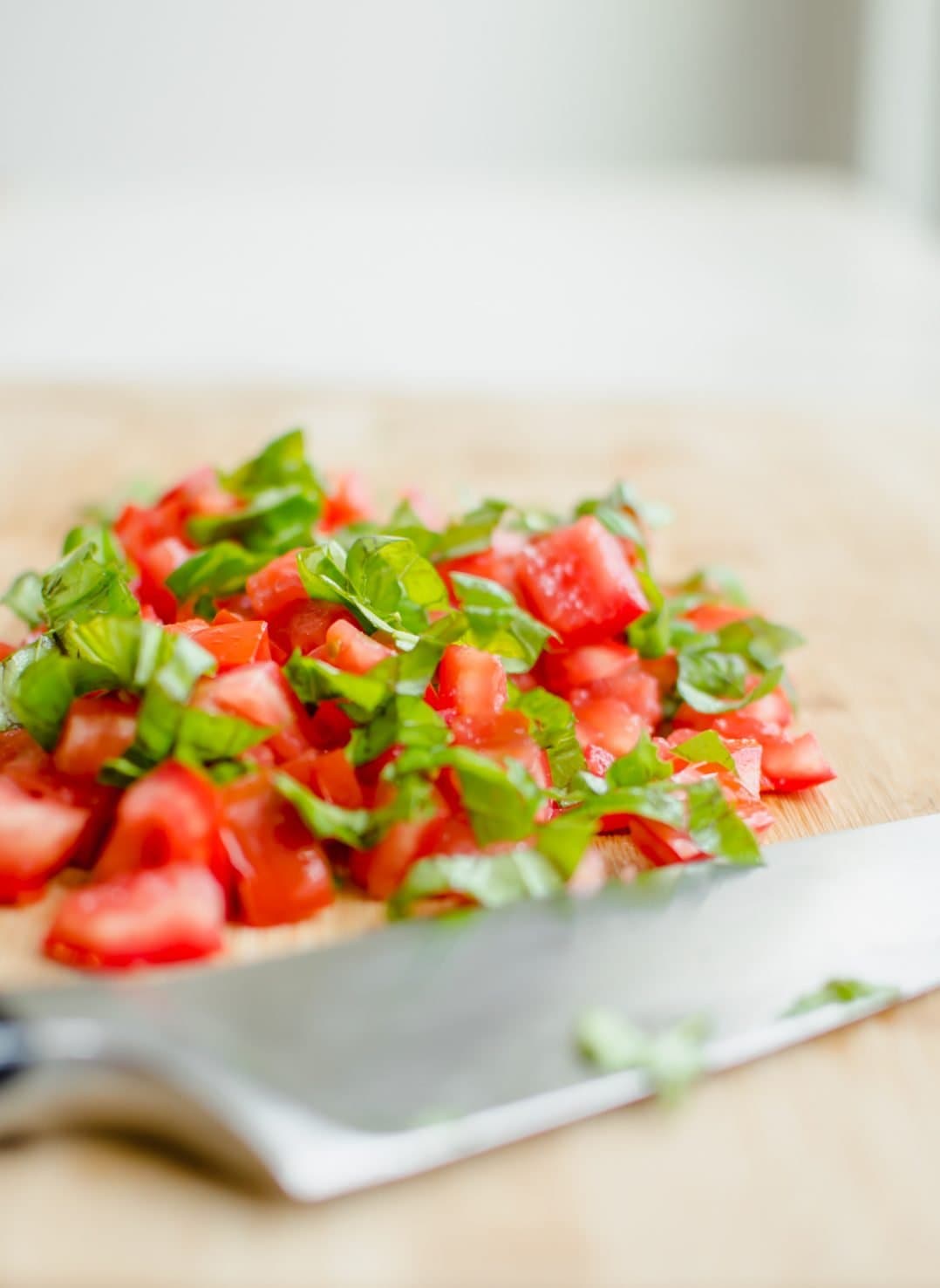 Sliced tomatoes and basil on a wooden cutting board with a knife on the side.