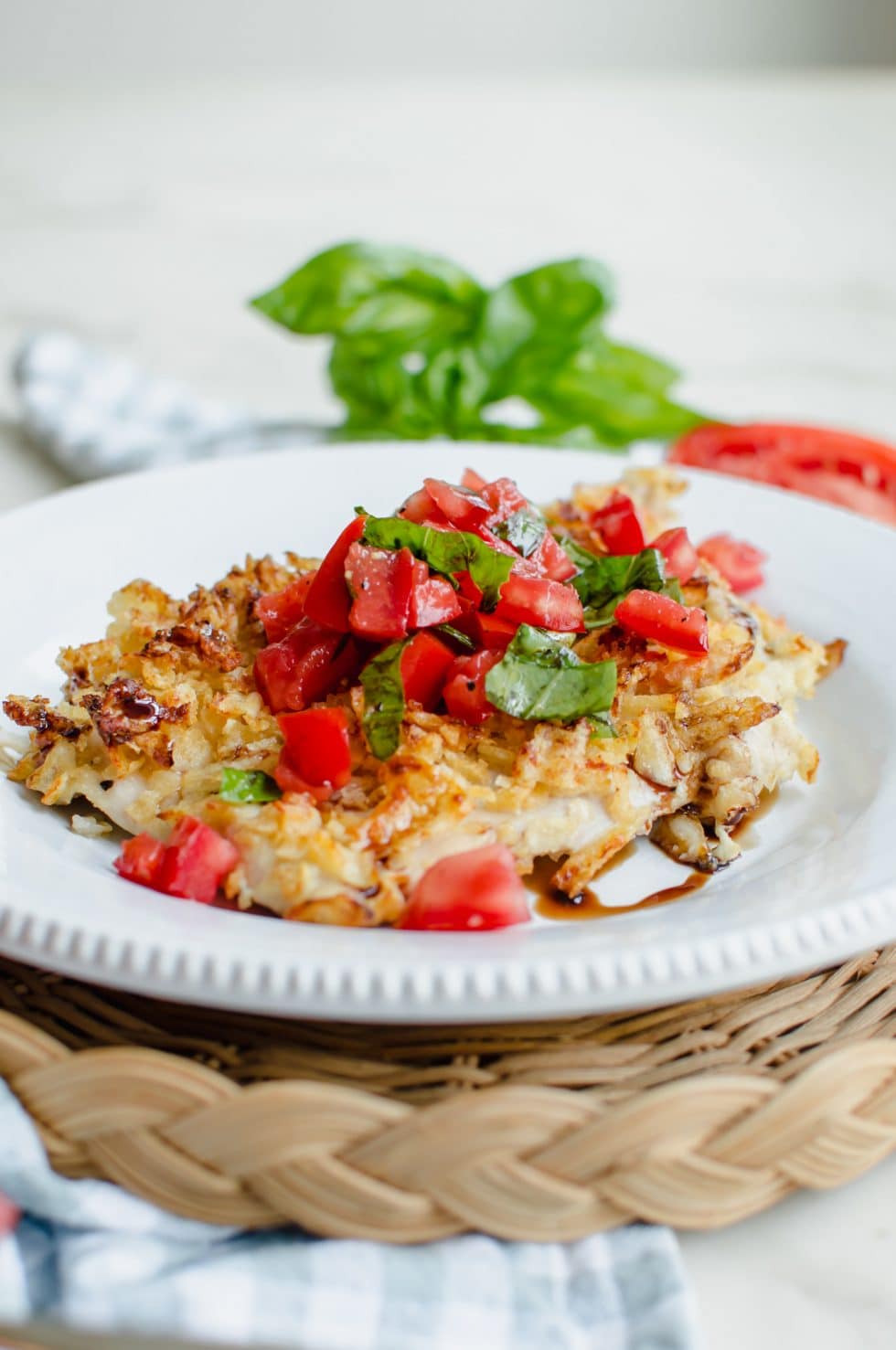 A side shot of a piece of potato chip chicken on a white plate topped with bruschetta topping.