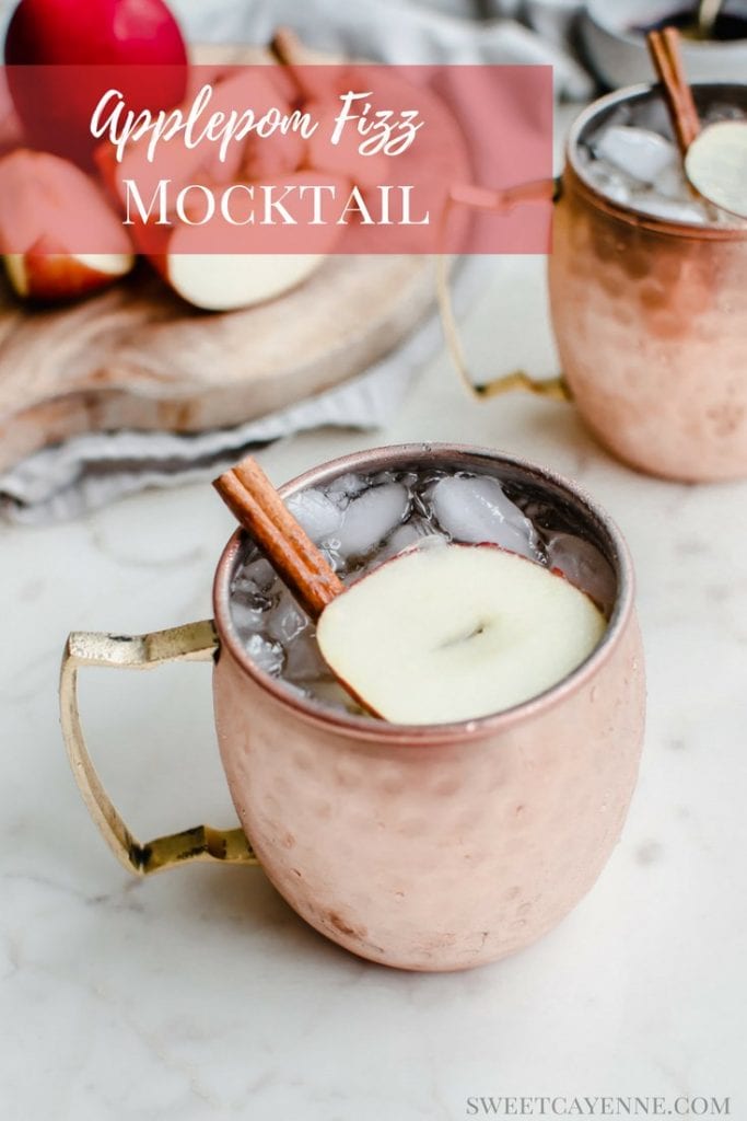 A moscow mule mug with a sparkling apple cider mocktail inside and a garnish of apple sliced and cinnamon stick.