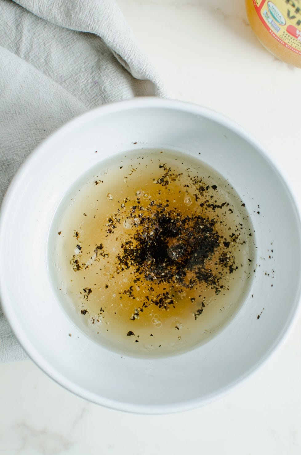 A white bowl with ingredients for tangy honey dressing inside.