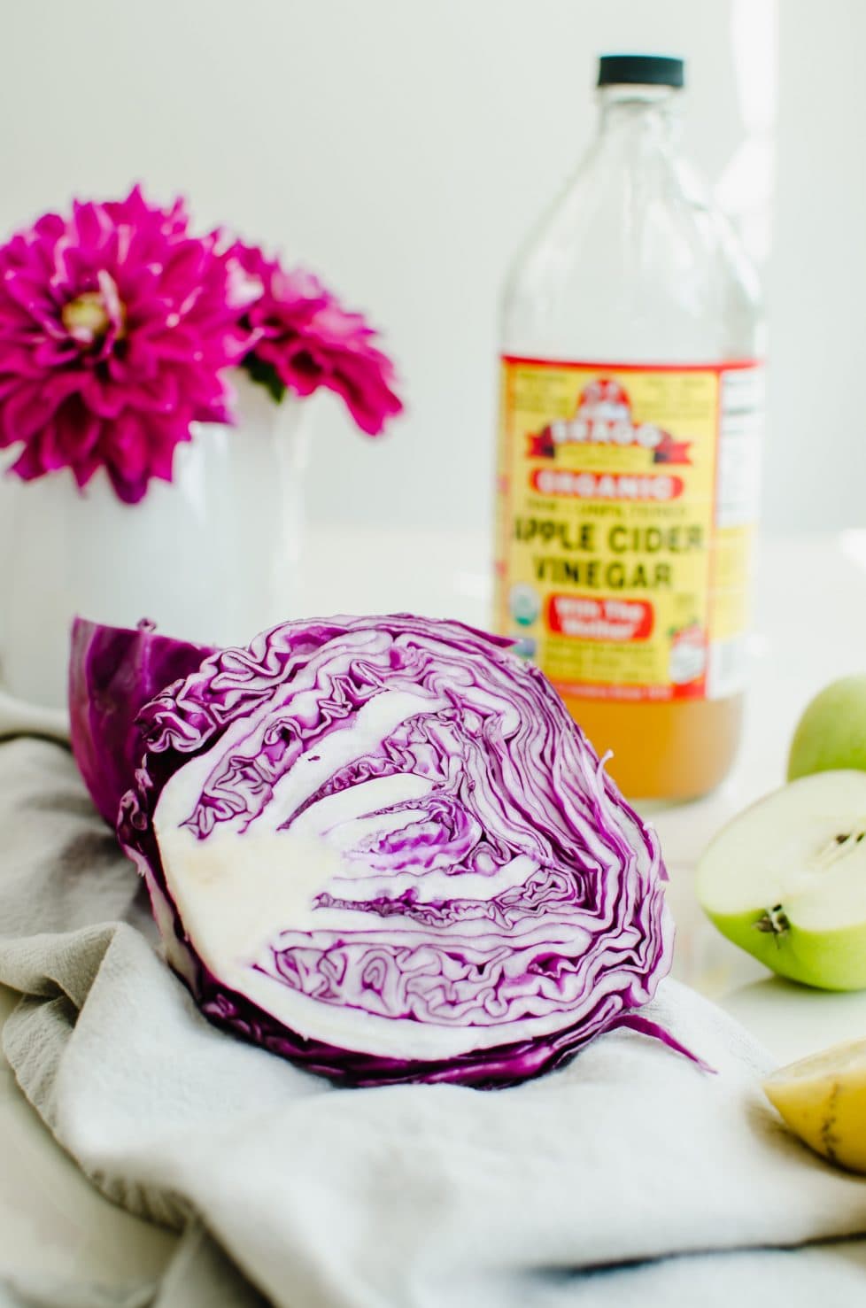 A red cabbage half with a green apple half on the side with a bottle of cider vinegar in the background.