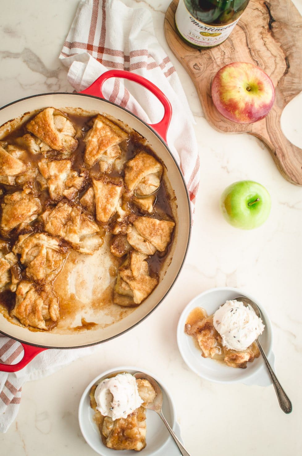 An overhead shot of apple dumplings in a red cast iron braised on a white counter top.