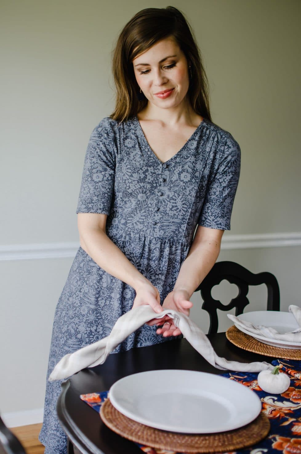 A woman tying a napkin to set at a place setting in a dining room. 