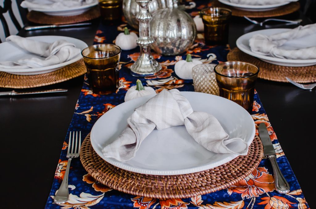 A napkin tied into a loose knot on a white plate with a rattan charger underneath.