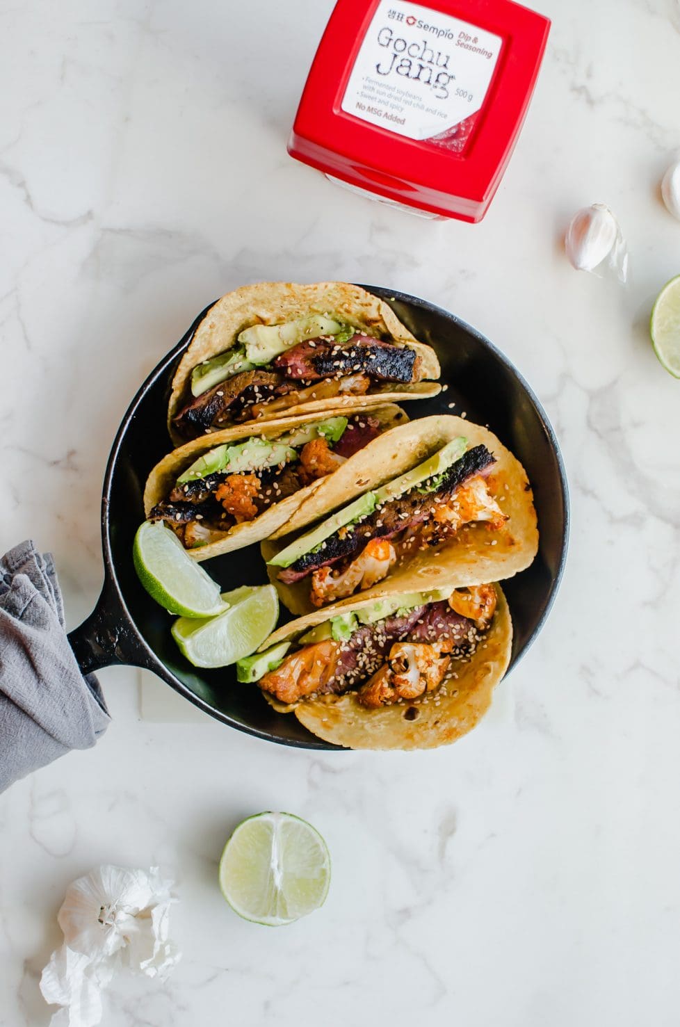 An overhead shot of a cast iron skillet filled with Korean-style beef tacos with roasted cauliflower. 