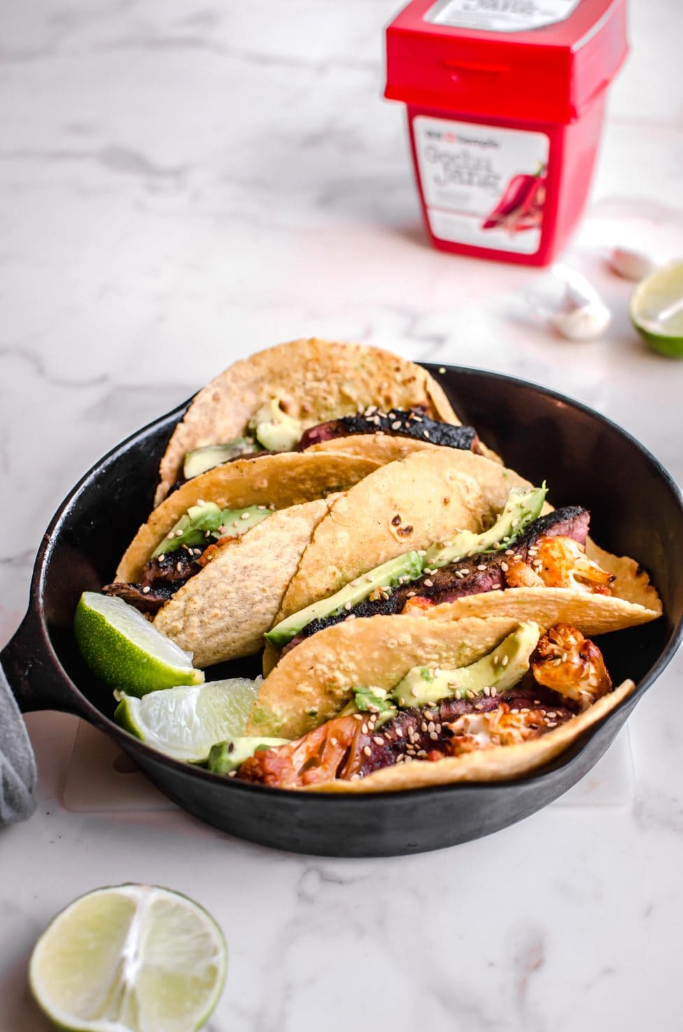 A side shot of tacos in a cast iron skillet with a box of gochujang sauce in the background. 