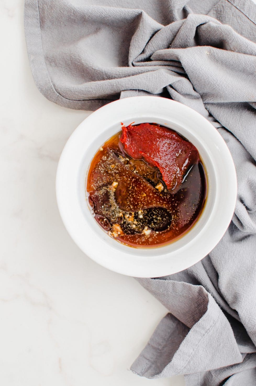 An overhead shot of a white bowl filled with gochujang Korean sauce and a grey tea towel.