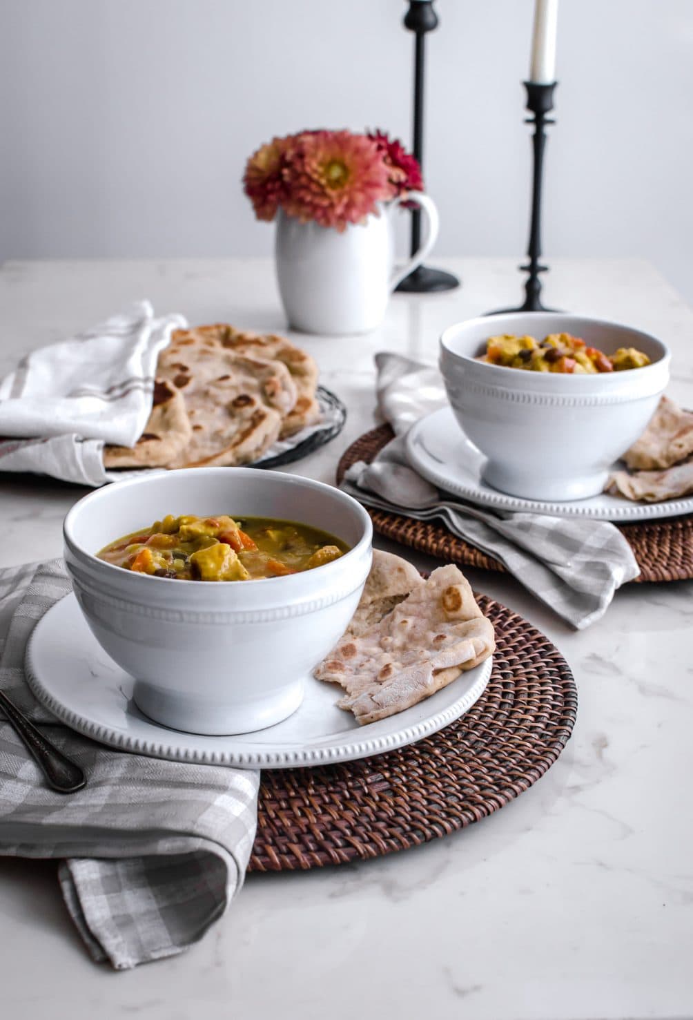 A white table with white bowls on rattan chargers with candles and Mango Chicken Curry.