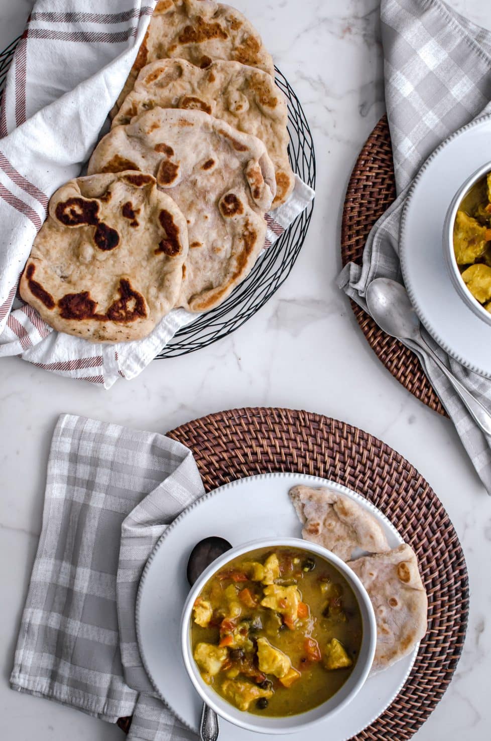 An overhead shot of a table set with rattan chargers and white bowls of Mango Chicken Curry. 