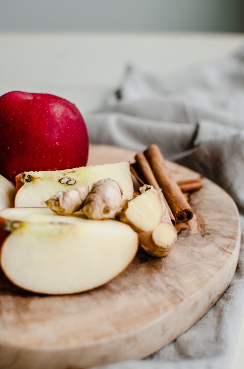 A cutting board with sliced apples, fresh ginger, cinnamon sticks, and 