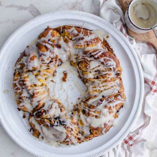 An overhead shot of a sweet potato cinnamon roll ring on a white platter with a plaid towel on the side.