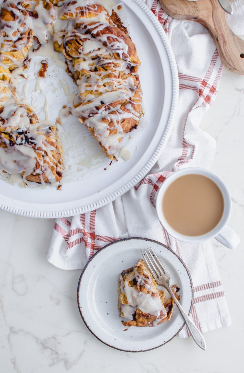 An overhead shot of a platter with an iced cinnamon roll ring on top and a cup of coffee on the side.