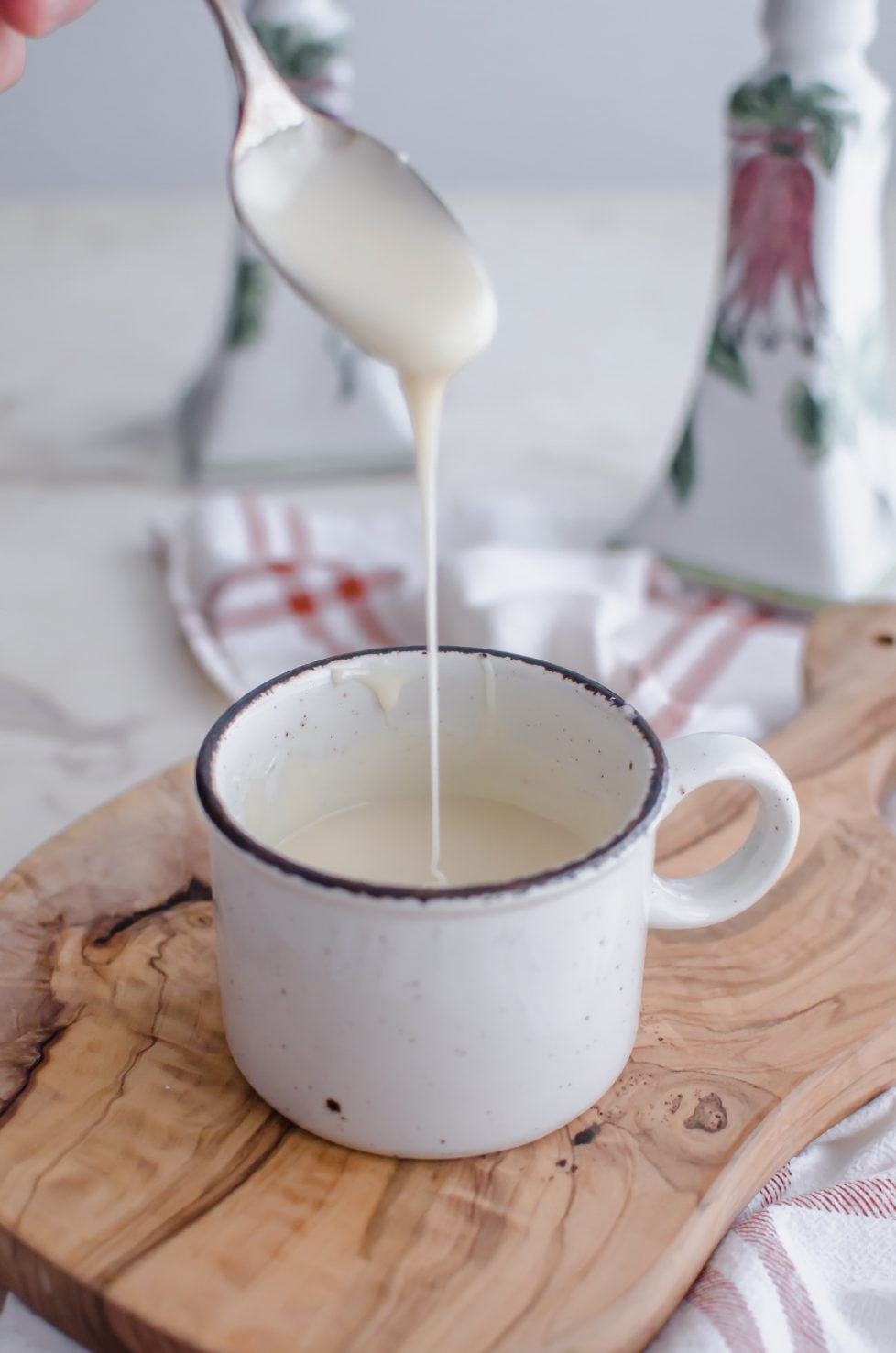 A white stone mug filled with maple glaze sitting on a cutting board. 