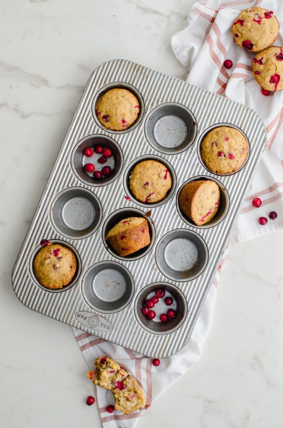 A muffin tin with some wells filled with cranberry cornbread muffins and some with fresh cranberries.