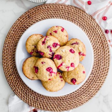 An overhead shot of a white plate on a rattan charger filled with cranberry cornbread muffins.