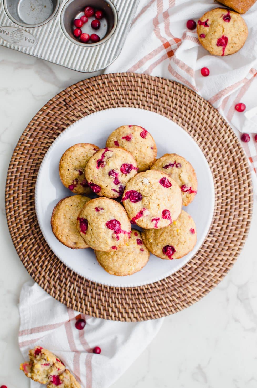 A white plate on a rattan charger filled with cranberry cornbread muffins.