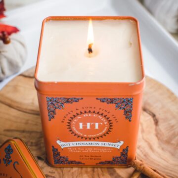 An overhead shot of a candle made in a tea tin sitting on a cutting board against a white background.