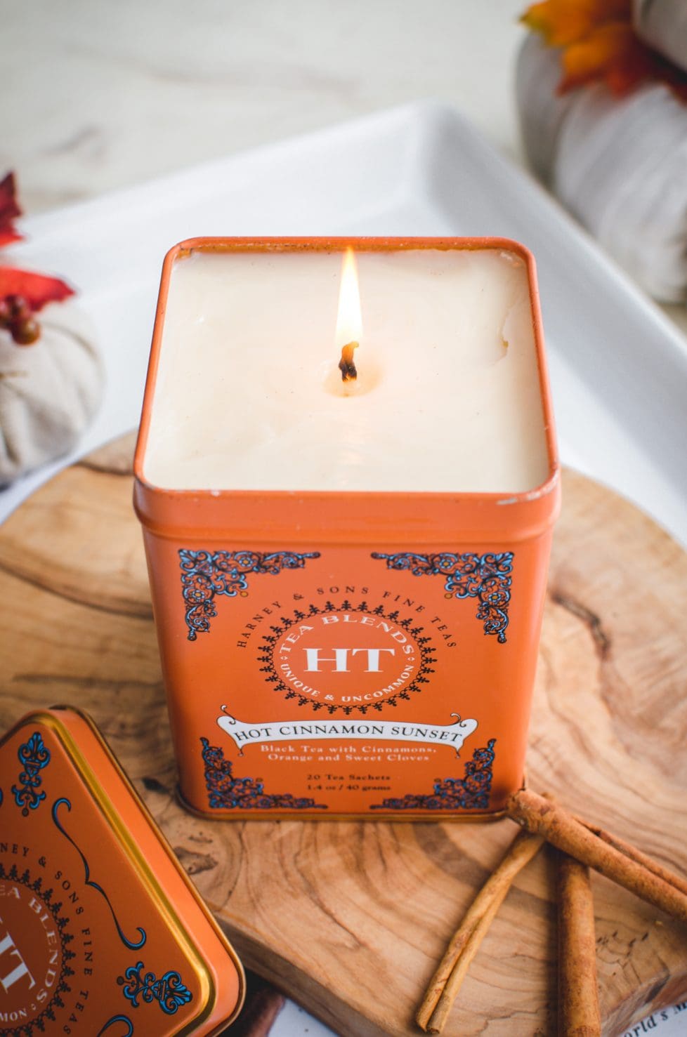 An overhead shot of a candle made in a tea tin sitting on a cutting board against a white background.