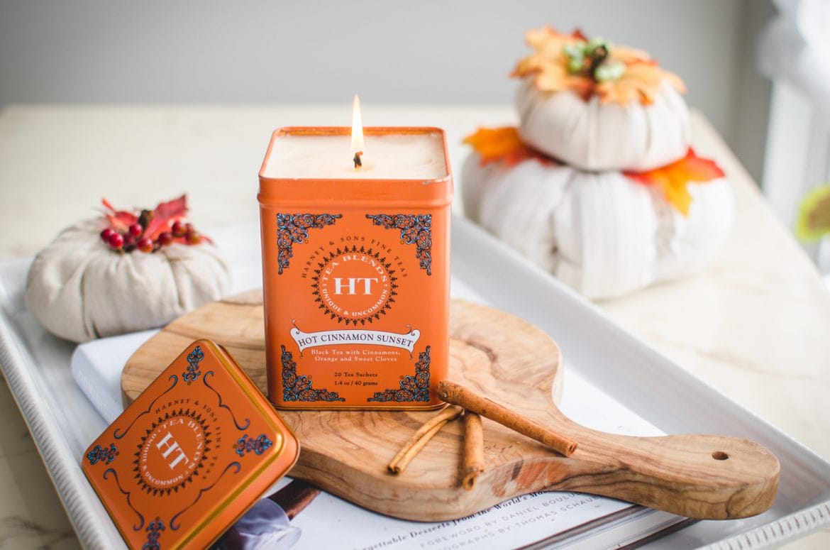 An straight-on shot of a candle made in a tea tin sitting on a cutting board against a white background.