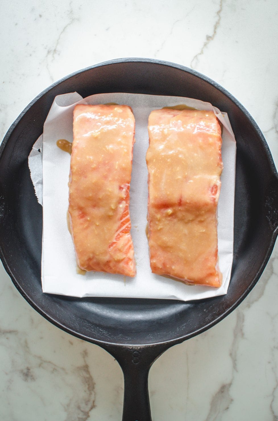 An overhead shot of raw salmon fillets in a cast iron skillet with miso maple glaze on top.