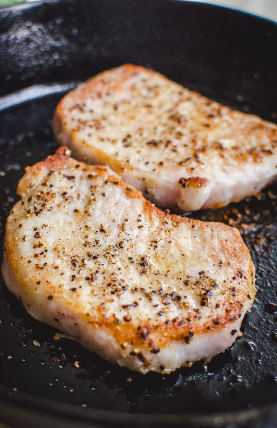 A side shot of sautéed pork chops in a cast iron skillet. 