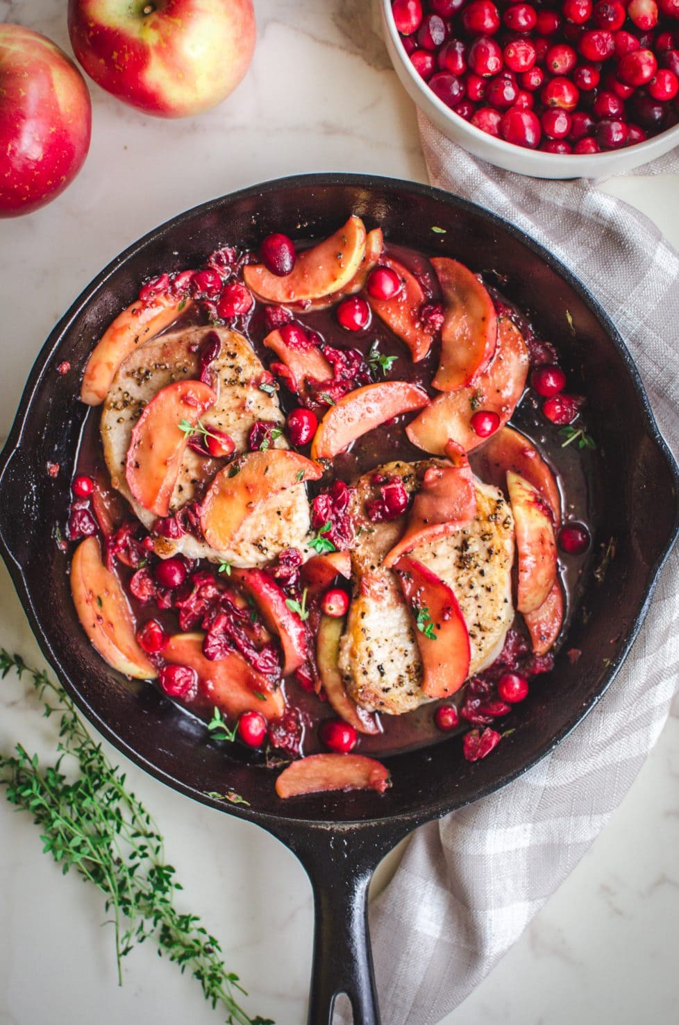 An overhead shot of pork chops in a skillet with a cranberry apple sauce.