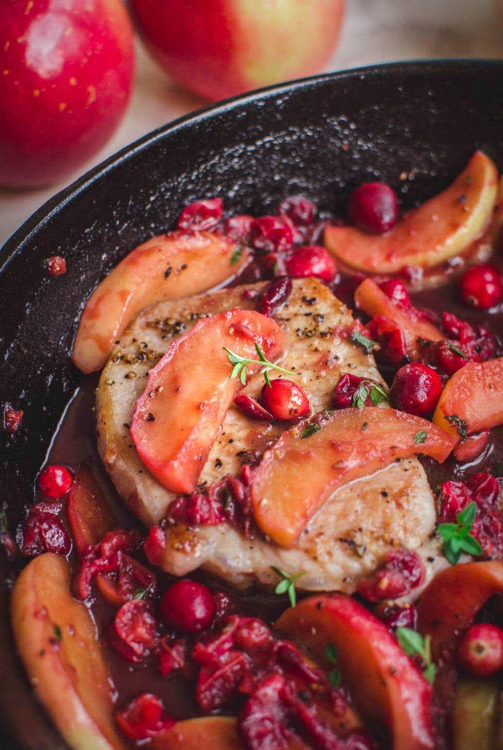 A close up shot of a pork chop in a skillet with apple cranberry sauce on top.