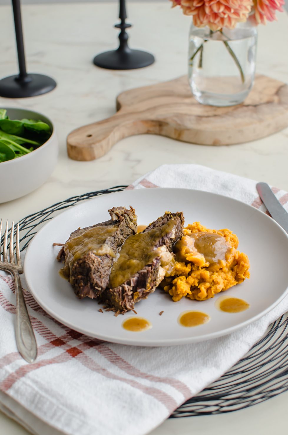 Beef roast on a plate with sweet potatoes and gravy.