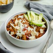An overhead shot of a stone bowl with steak chili and topped with cheese and avocado.