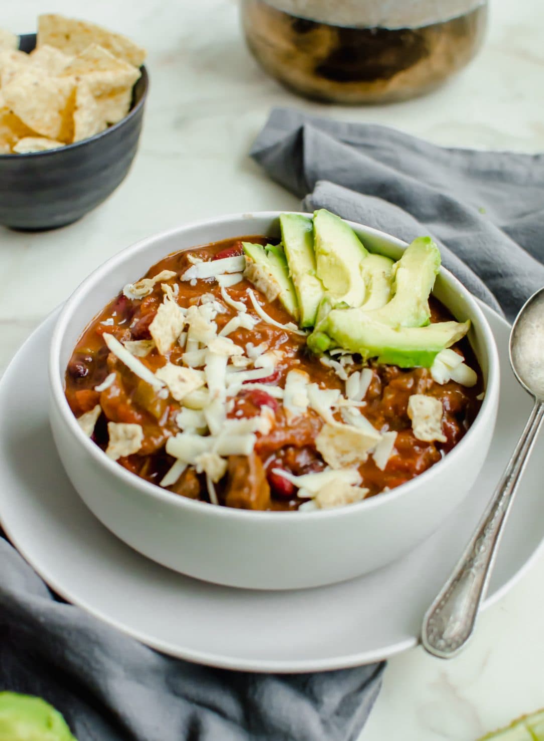 An overhead shot of a stone bowl with steak chili and topped with cheese and avocado.