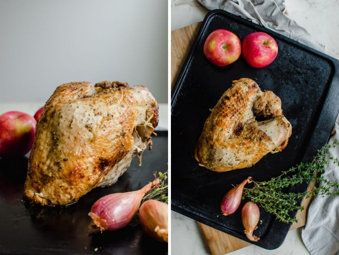 A cooked bone-in turkey breast on a baking sheet with apples, shallots, and thyme on the side. 