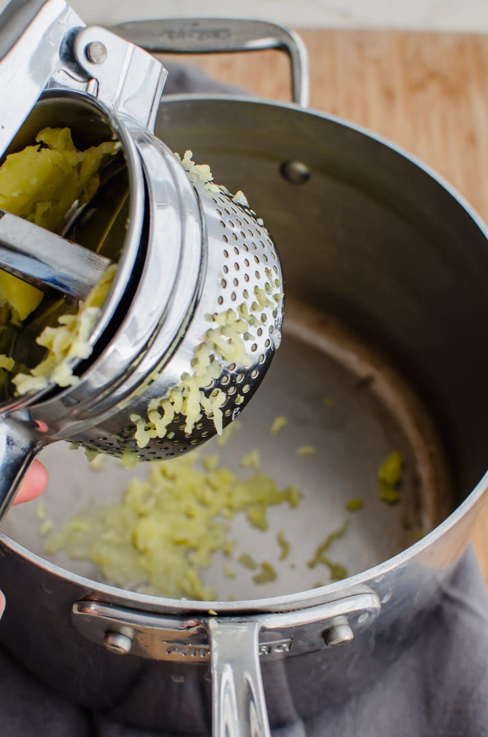 A potato ricer ricing gold potatoes into a mixing bowl.