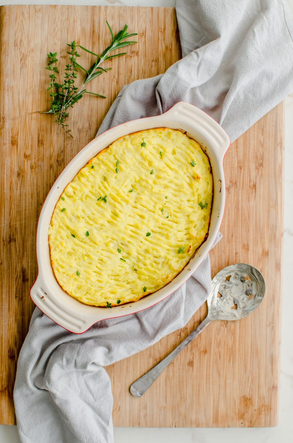 A casserole dish filled with Duchess potatoes sitting on top of a grey tea towel and cutting board. 