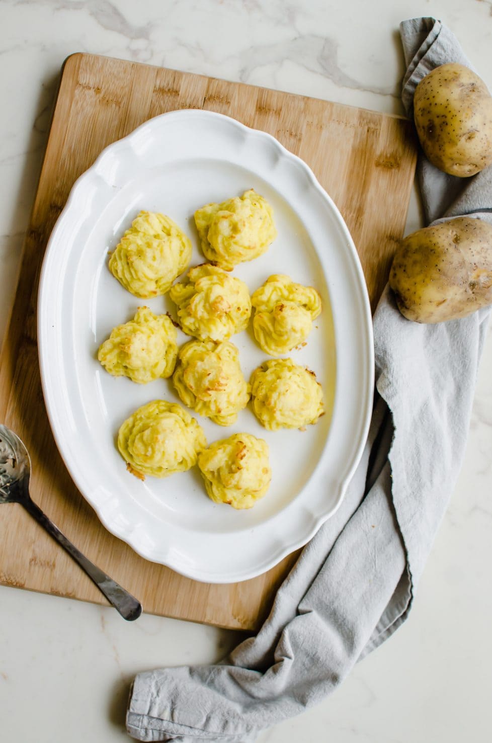 A white platter with piped Duchess potatoes on top and a grey tea towel on the side.