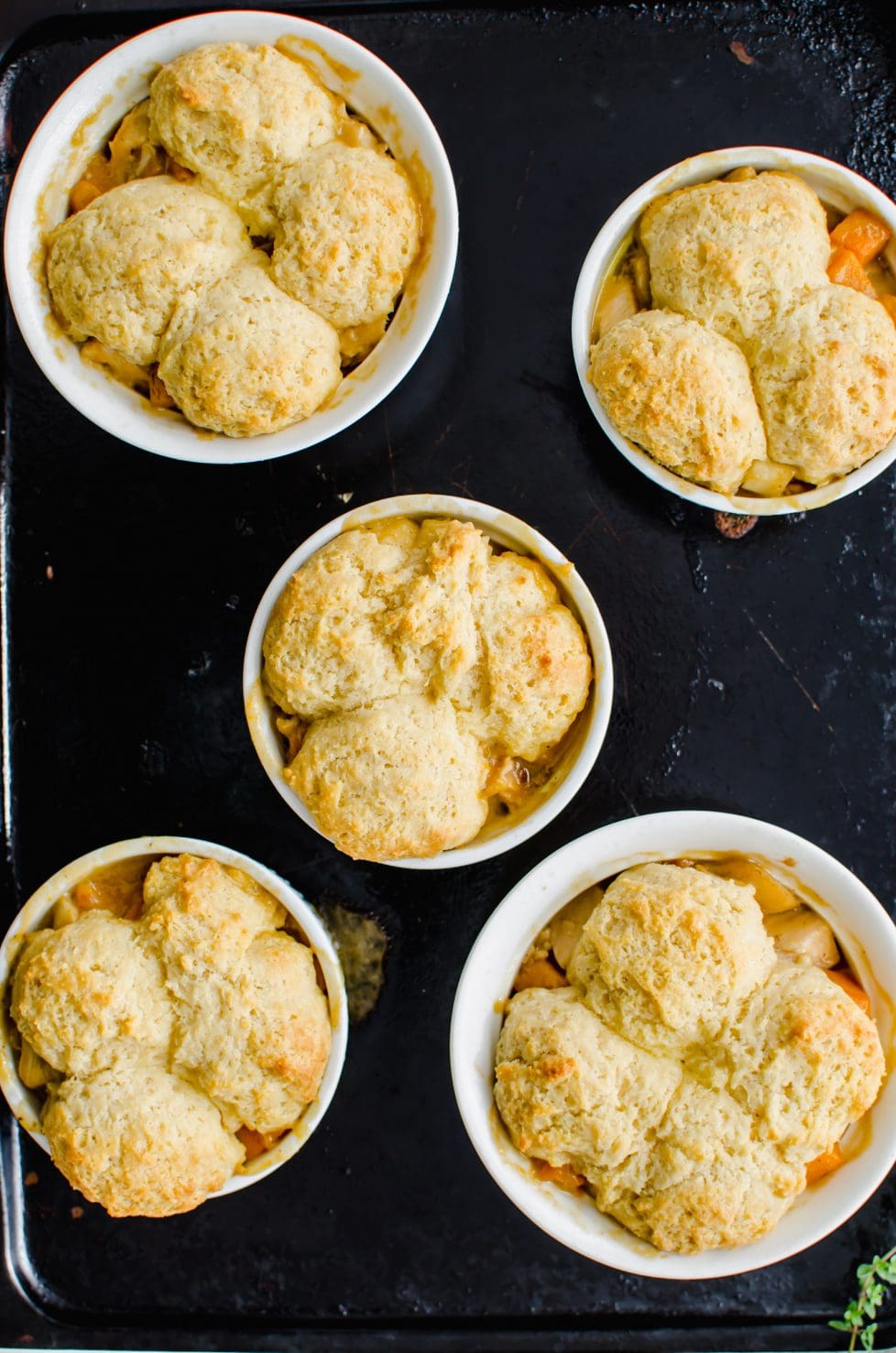 An overhead shot of a dark baking sheet with ramekins of turkey pot pie on top.