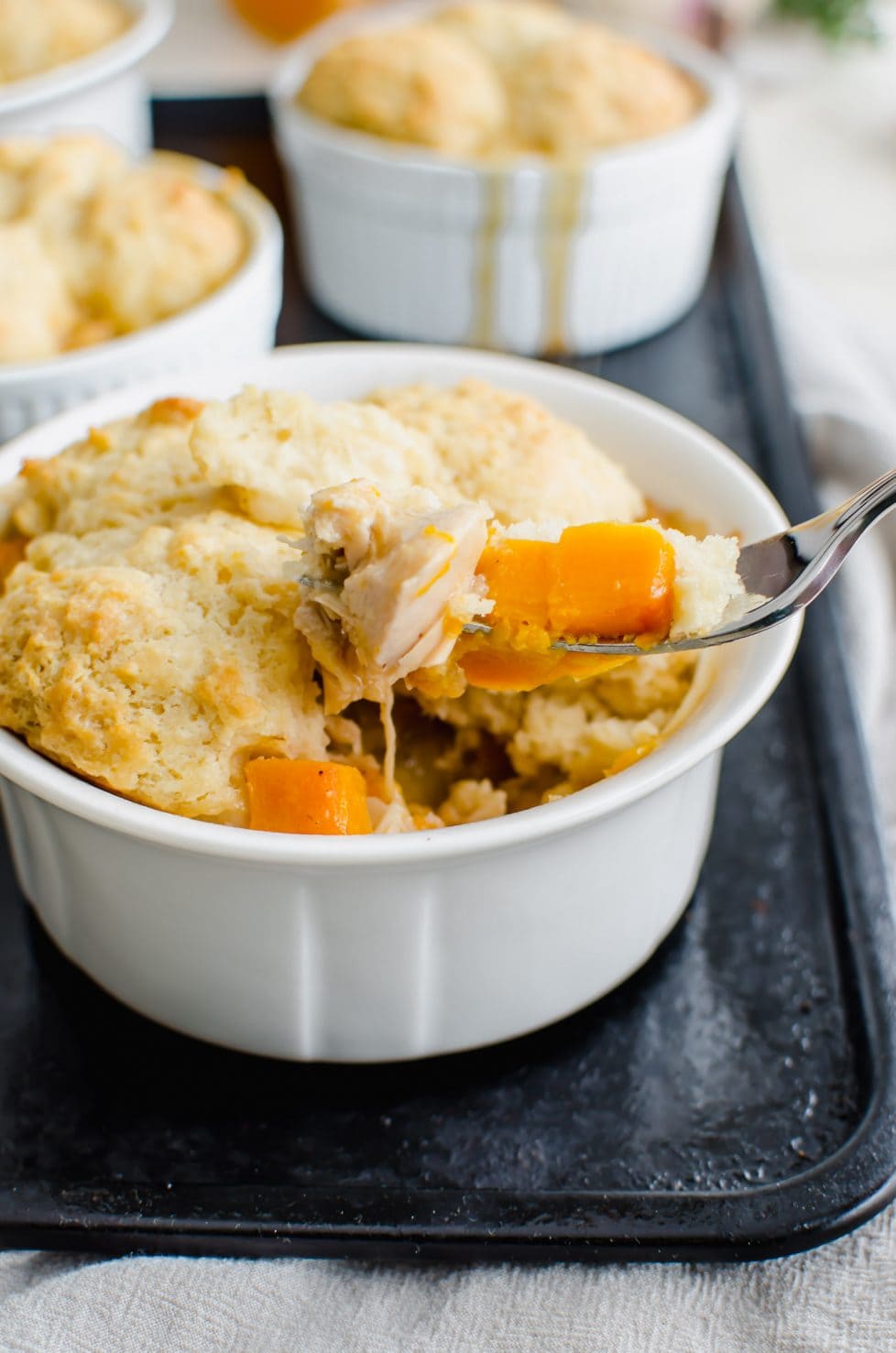 A white ramekin filled with turkey pot pie and drop biscuit topping and a fork lifting up a bite.