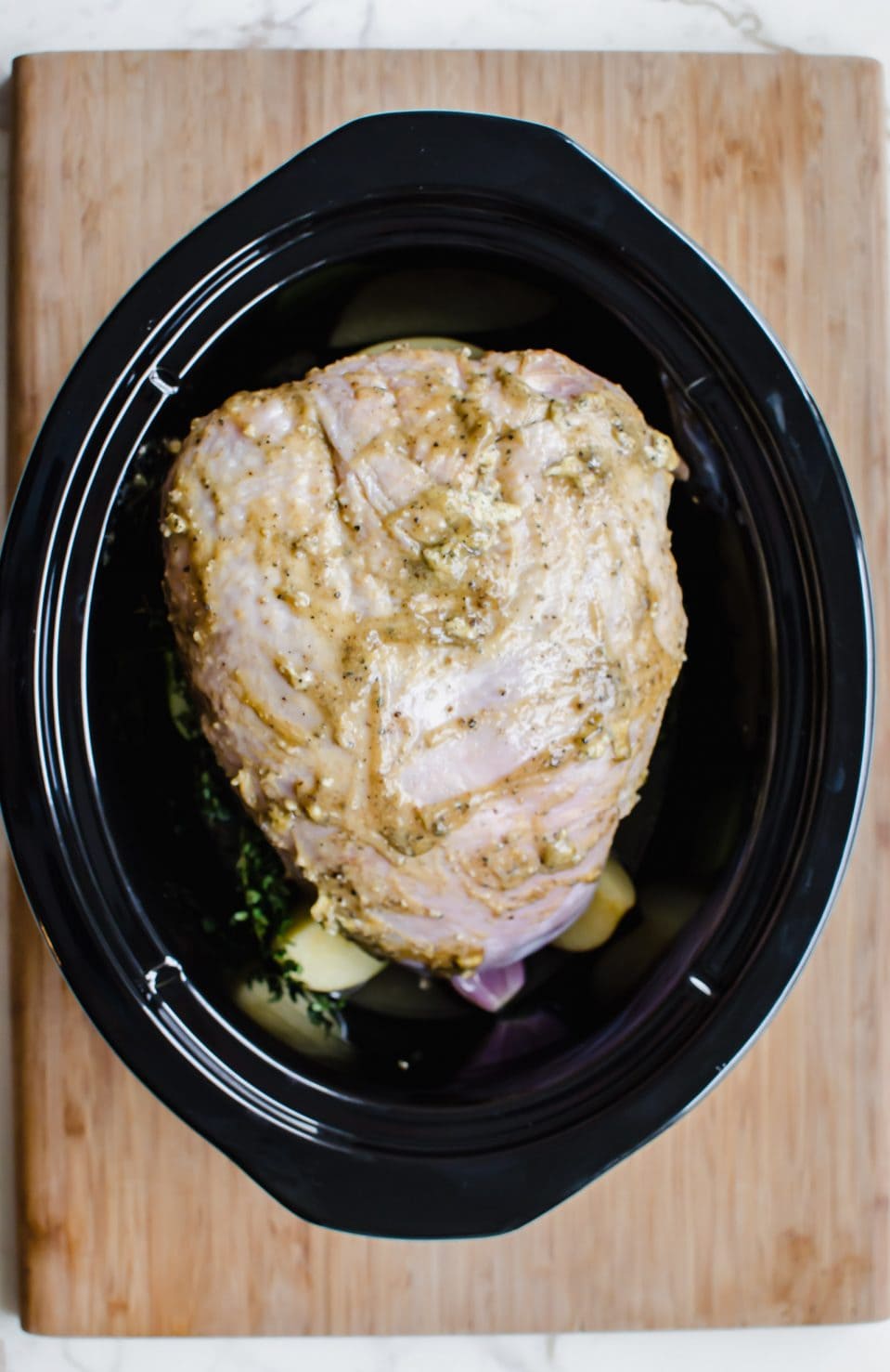 A raw, rubbed turkey breast inside a black slow cooker. 