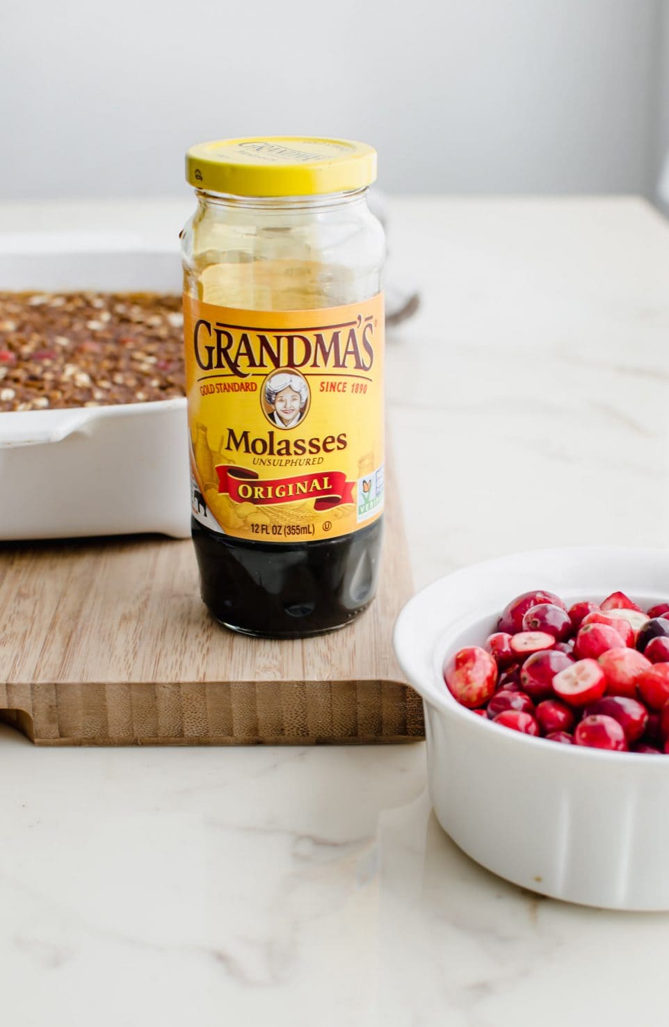 A bottle of Grandma's molasses next to a bowl of cranberries and gingerbread baked oatmeal.