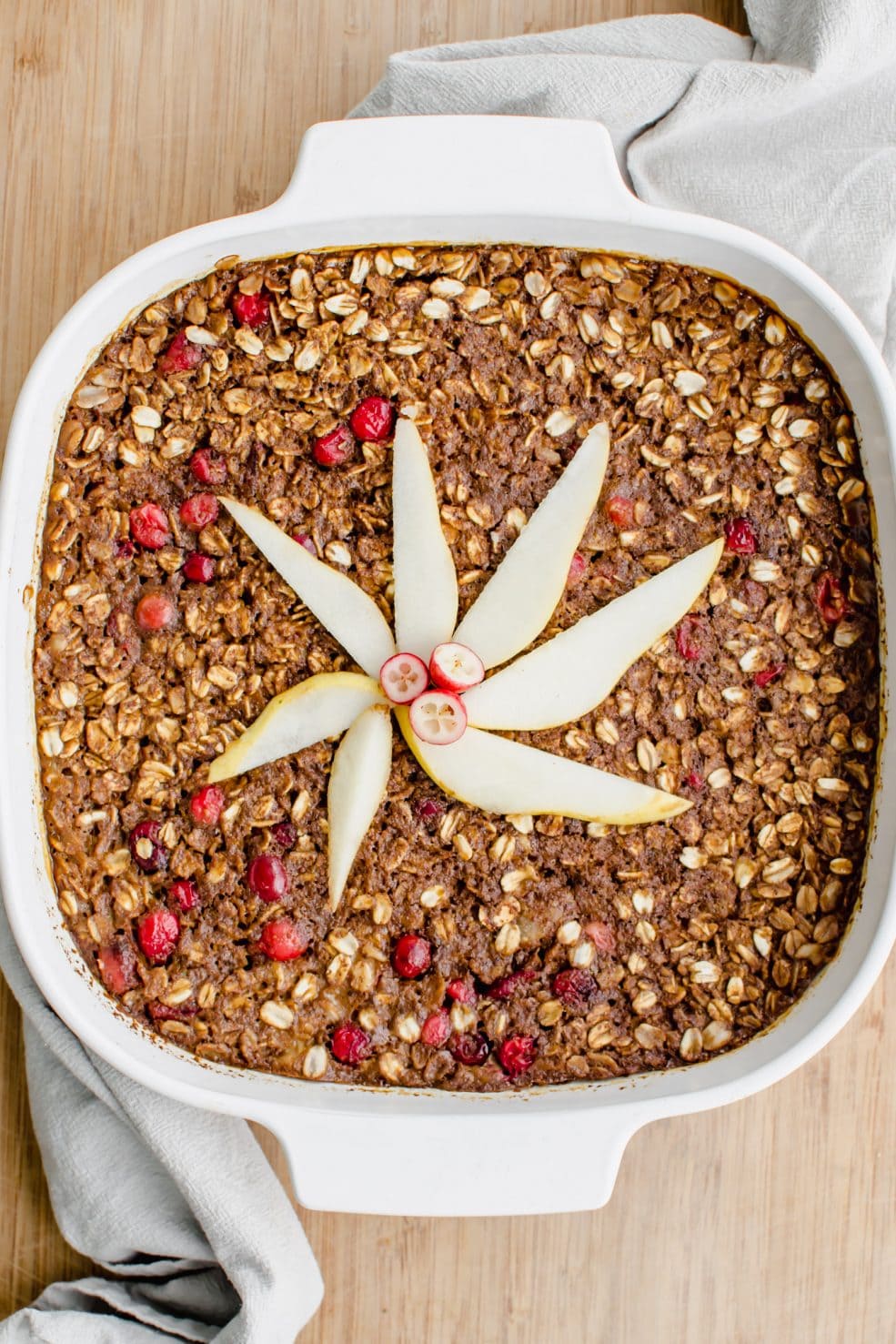 A white casserole dish filled with gingerbread baked oatmeal and topped with pear slices.