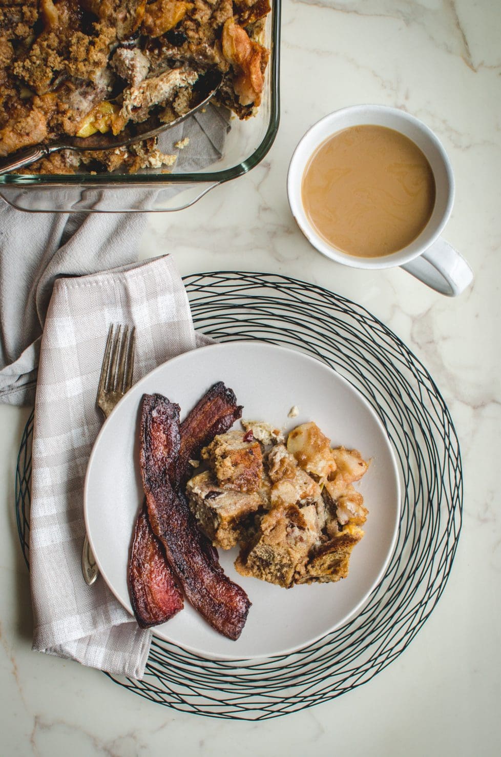A plate with bacon and bread pudding next to a cup of coffee.