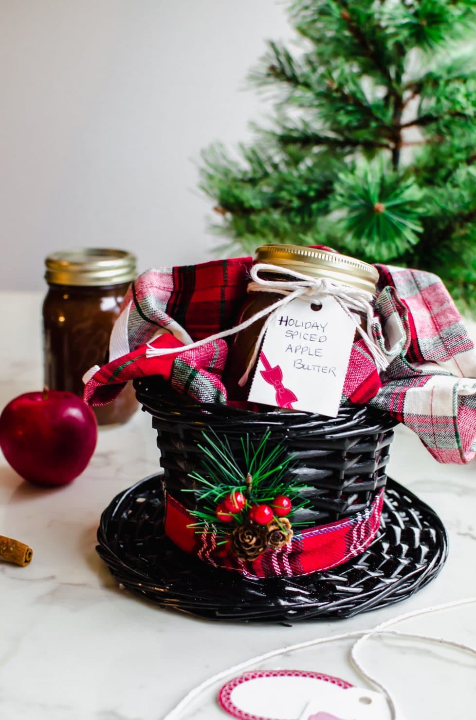 A basket shaped like a black hat with a plaid dish towel and jar of apple butter inside. 