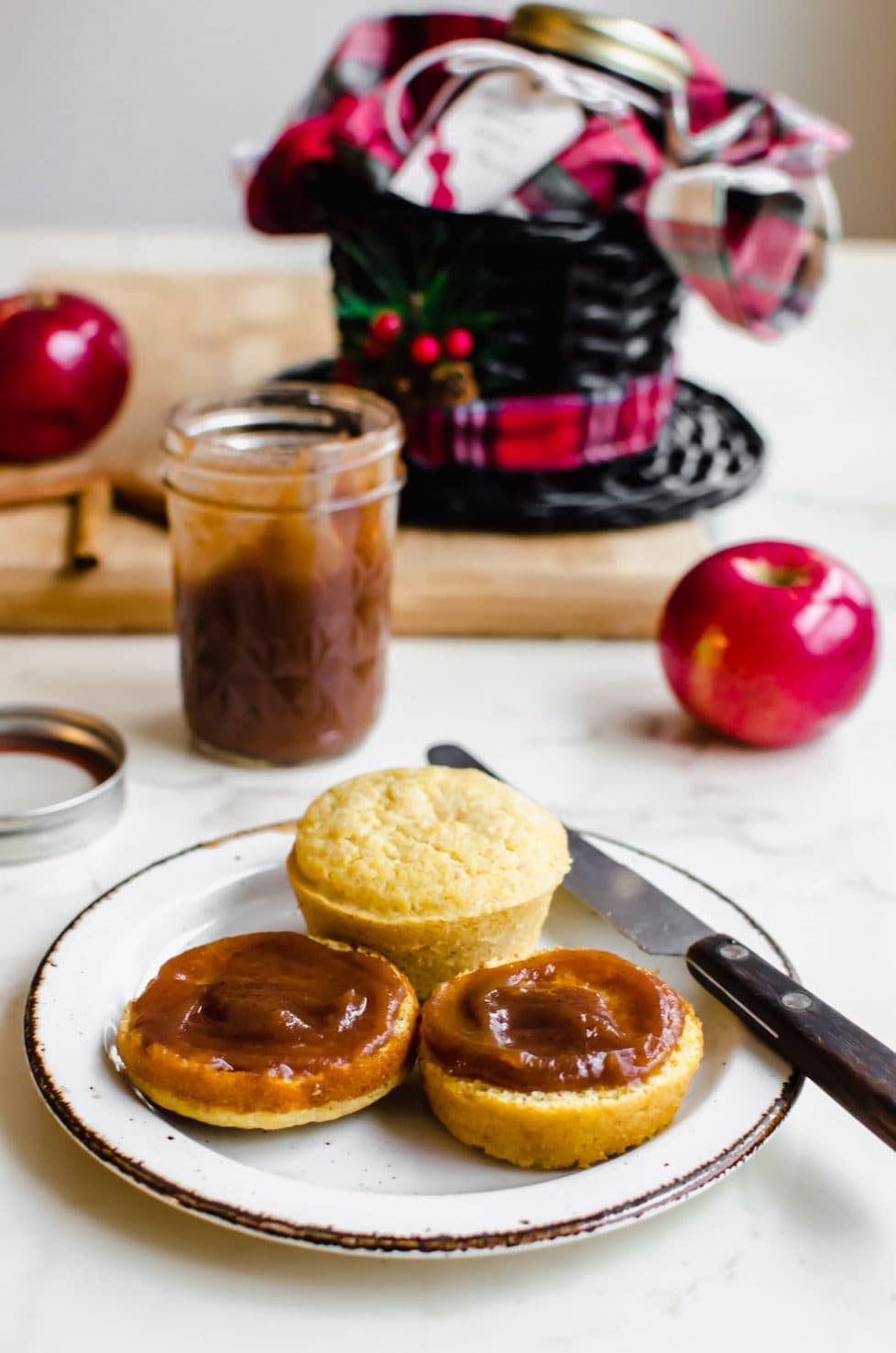 A white plate with a cornbread muffin sliced open and smeared with apple butter.