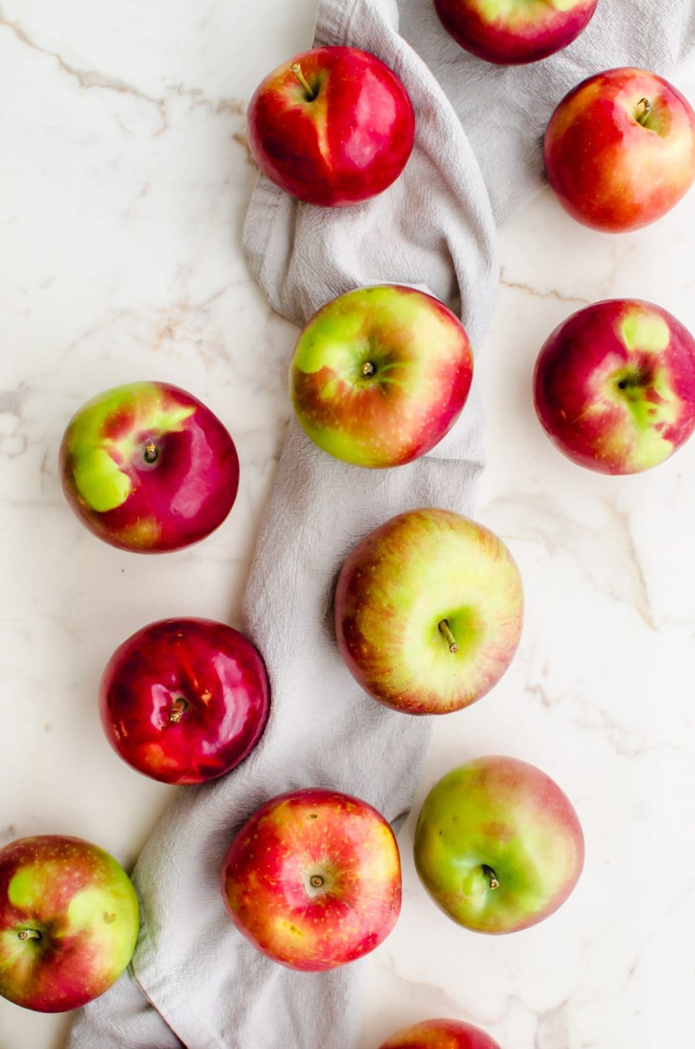 An overhead shot of a bunch of apples sitting on a light grey dish towel. 