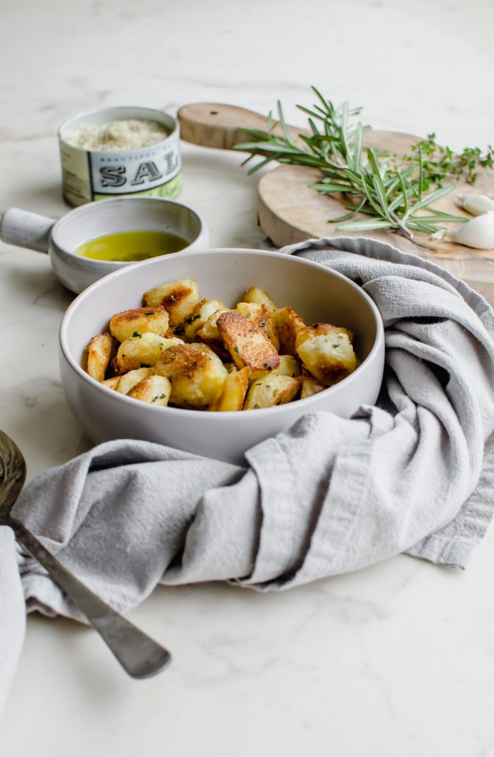 A grey bowl filled with crispy roasted potatoes with bowls of salt and olive oil on the side.