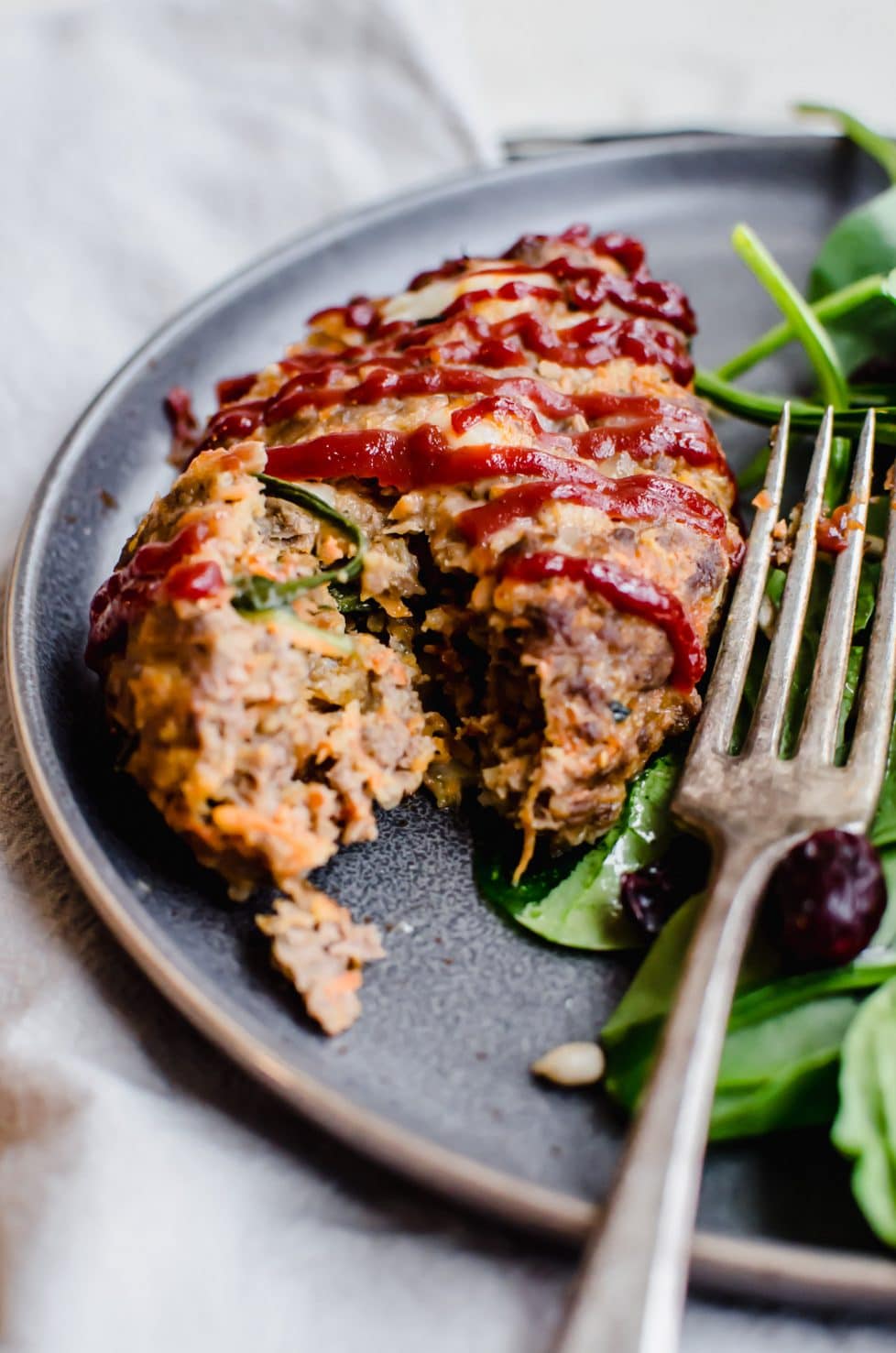 A grey plate with a mini meatloaf and spinach salad with a fork taking a bite out of the meatloaf.