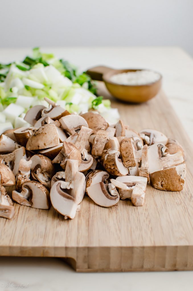 A cutting board topped with chopped mushrooms, bok choy, and a container of miso paste.