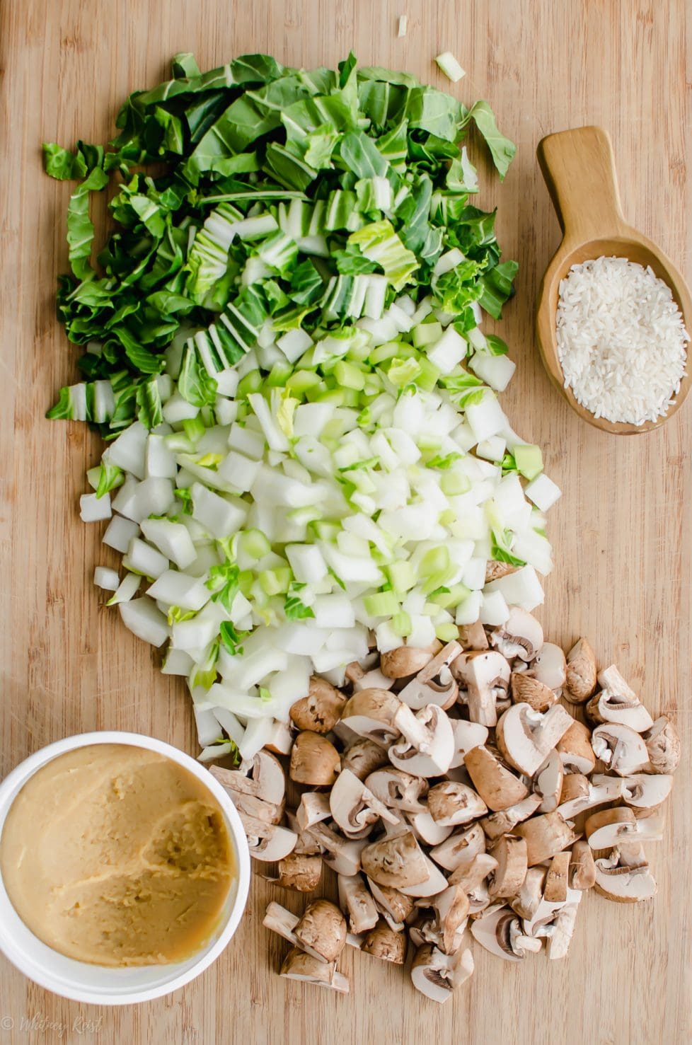 A cutting board topped with chopped mushrooms, bok choy, and a container of miso paste. 