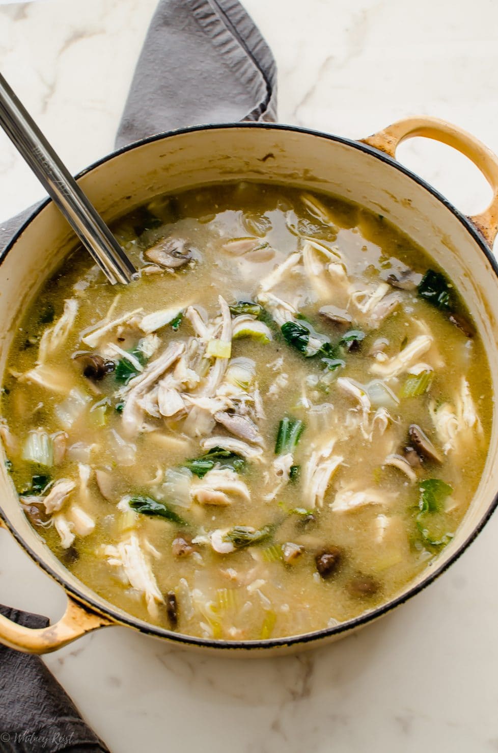 A yellow Dutch oven filled with Miso Chicken and Rice Soup and a ladle. 